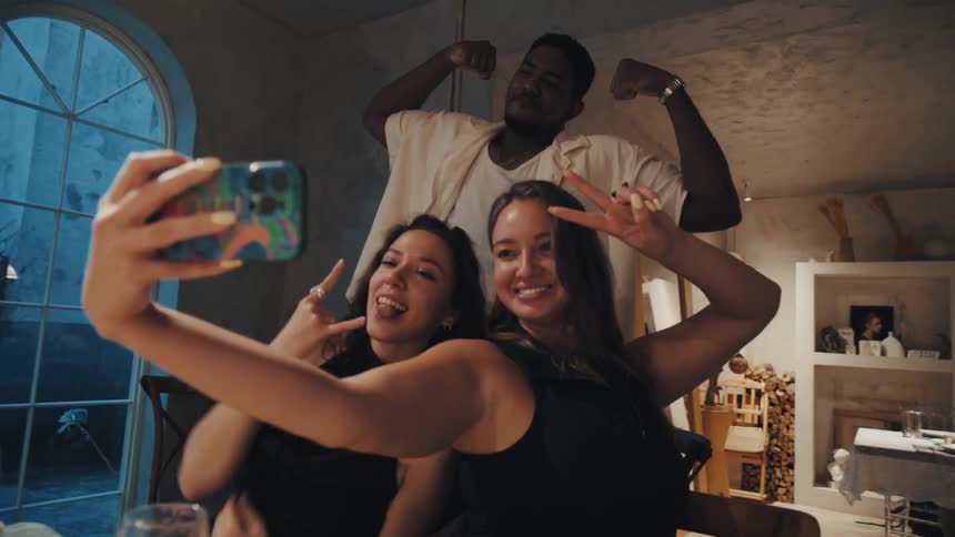 A group of diverse friends make funny faces and pose for a selfie on a smartphone during a dinner party in slow motion