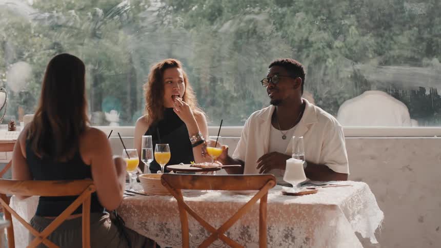 A diverse group of happy friends talk and laugh together while enjoying brunch in a sunlit cafe