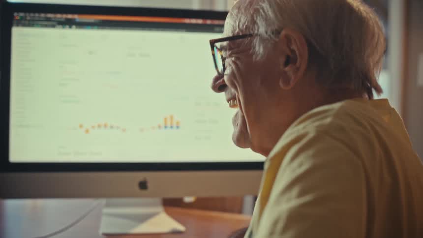 A happy elderly man smiles while successfully managing his finances online from his home office computer