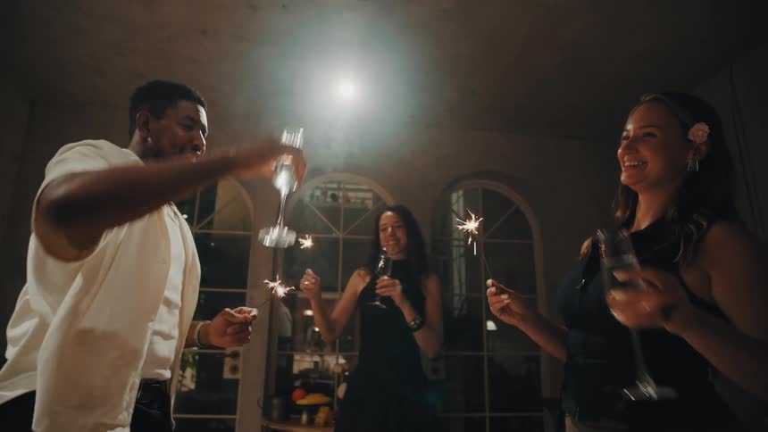 A group of diverse friends joyfully celebrate at a house party, toasting with champagne and dancing with lit sparklers in slow motion