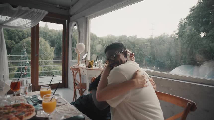 In slow motion, a loving interracial couple hugs tightly at a dinner party with friends in a beautiful restaurant