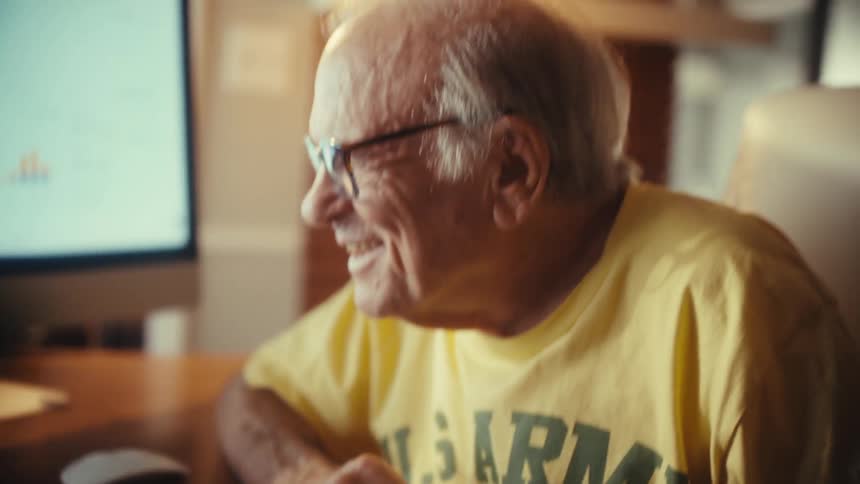 An elderly man smiles with satisfaction while working on his finances at his home office computer