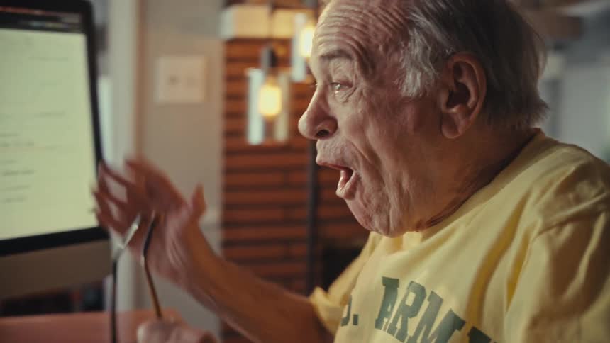 An astonished senior man removes his glasses in disbelief as he sees positive results on his computer monitor