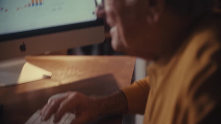 Close up of a smiling elderly man analyzing financial data on his computer in a warm home office setting