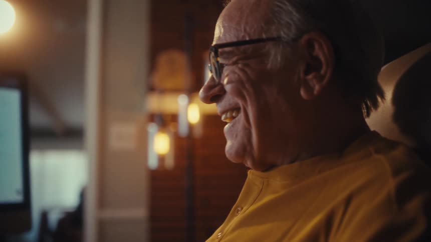 Happy elderly man in glasses smiles with satisfaction while working late from his home office, pleased with the results on his computer