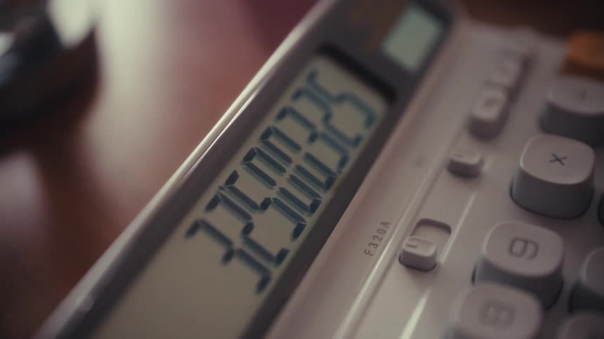 An extreme close-up shot of a calculator's digital display as someone calculates figures