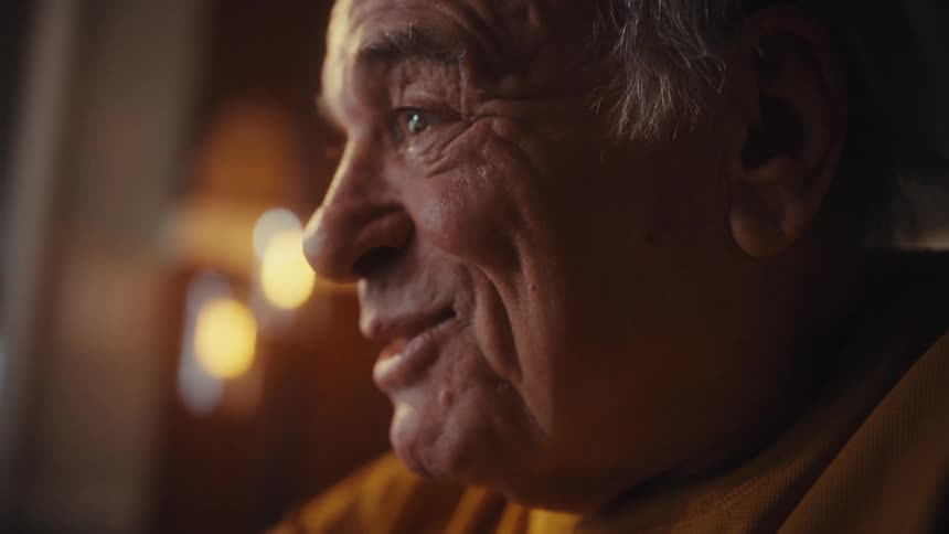 A smiling senior man works late from his home office, analyzing financial data on his laptop and computer monitor