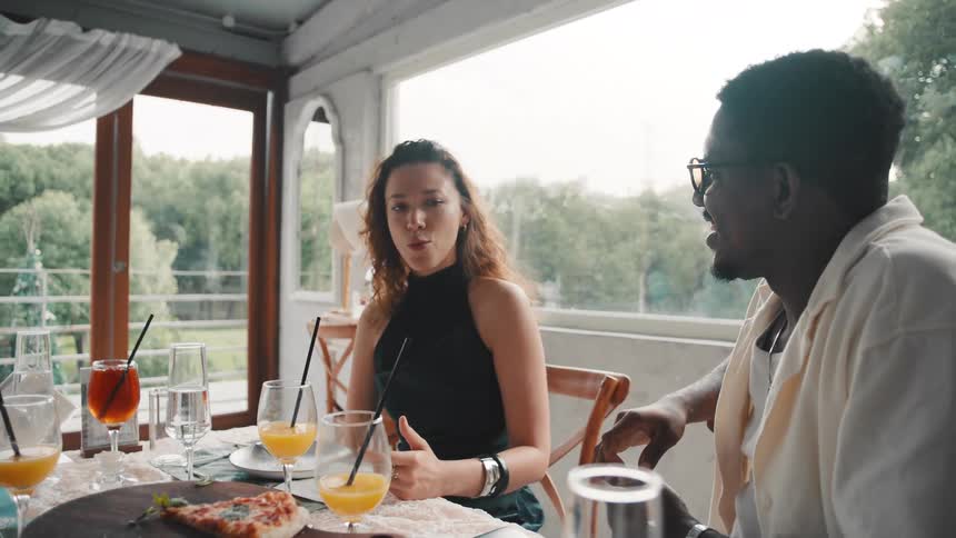 A diverse group of friends laughs and enjoys conversation while dining together at a beautiful restaurant in slow motion