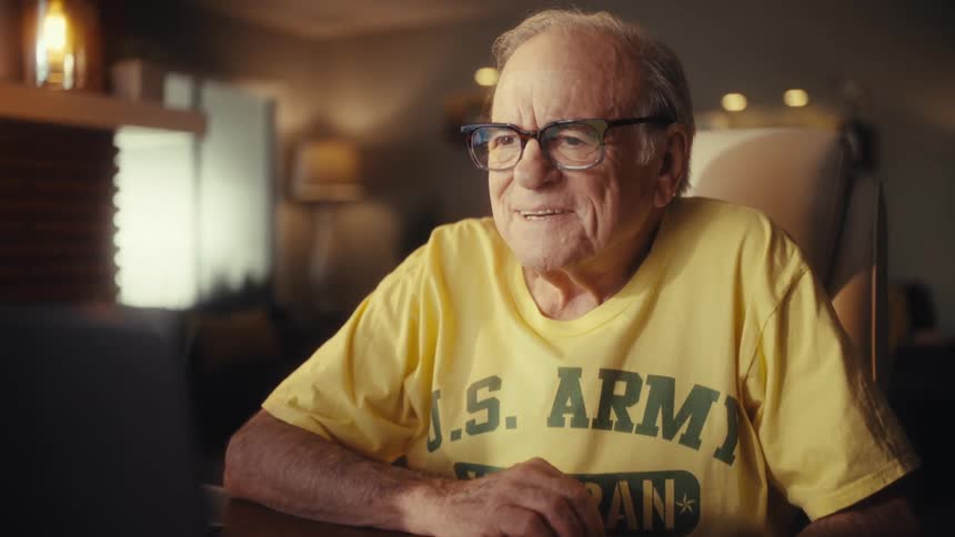 Joyful senior Army veteran waves and laughs during a heartwarming video call at home