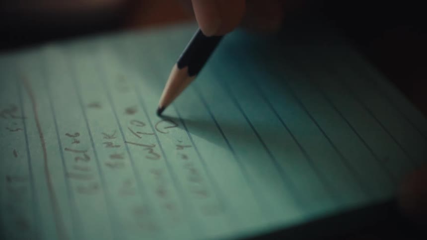 Close up of a hand with a pencil writing a to do list on a notepad next to a calculator