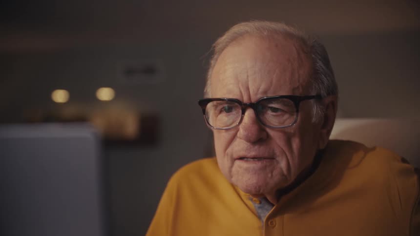 A close-up shot captures the changing expressions of a senior man, from happy to concerned, as he watches his laptop screen at night