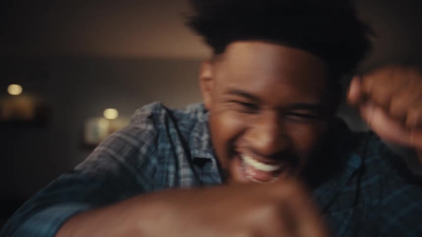 A jubilant man celebrates enthusiastically, pumping his fists and playfully punching towards the screen