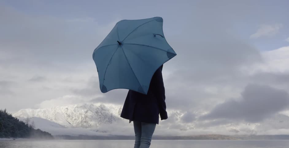 A woman spins an umbrella while looking at a mountain lake in the winter