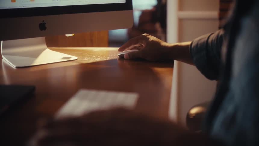 A close-up shot of a person's hands typing on a wireless keyboard and using a mouse while working at a desk