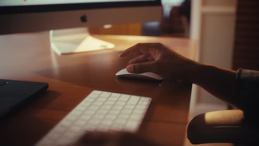 Close-up slow-motion shot of hands typing on a keyboard and then using a computer mouse on a wooden desk