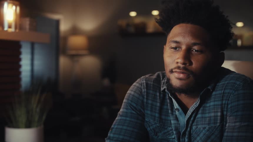 A focused African American man works late at night in his modern home office, analyzing data and charts on his computer