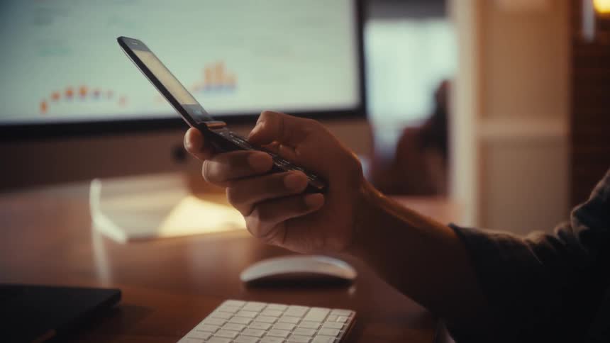 A person sitting at a desk flips open a vintage mobile phone and starts texting