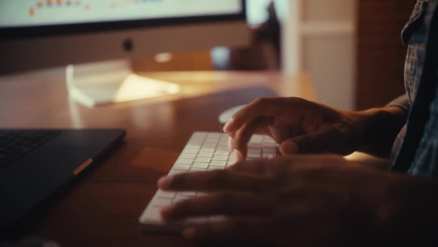 Cinematic close-up of a person's hands typing on a wireless keyboard at a modern desk