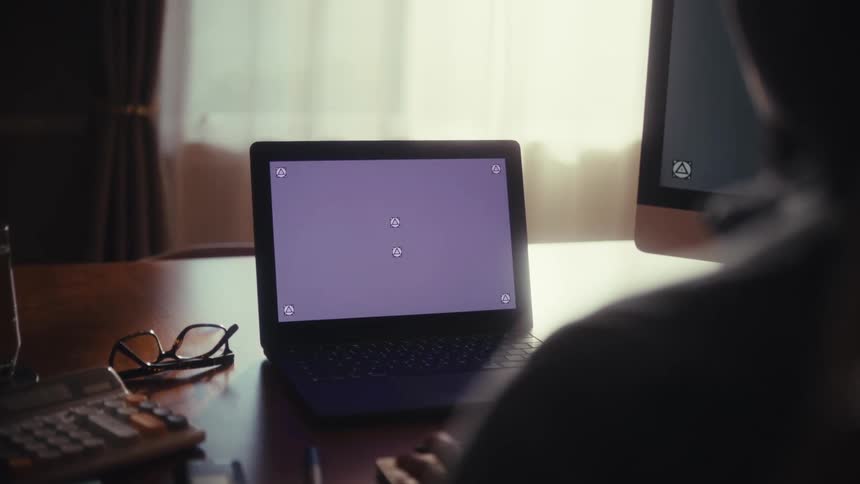 An over-the-shoulder shot of a person at a desk with a laptop screen displaying tracking markers for compositing
