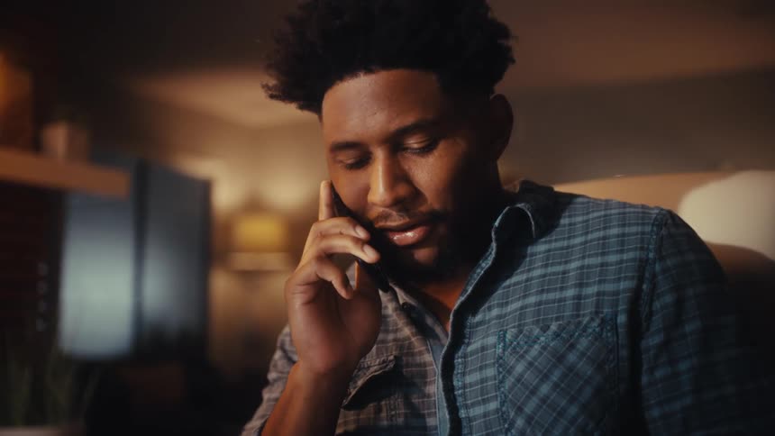 Close up of a young man talking on a flip phone at his desk in a warm, atmospheric room at night