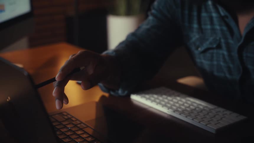 Focused businessman analyzes financial data charts on his computer screens while working late in a modern home office