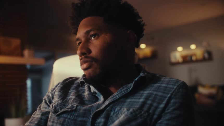 A focused man works late at his desk in a dimly lit home office as the camera slowly pushes in on his thoughtful expression