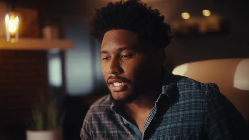 An expressive young man passionately discusses work on a video call from his warmly lit modern home office at night