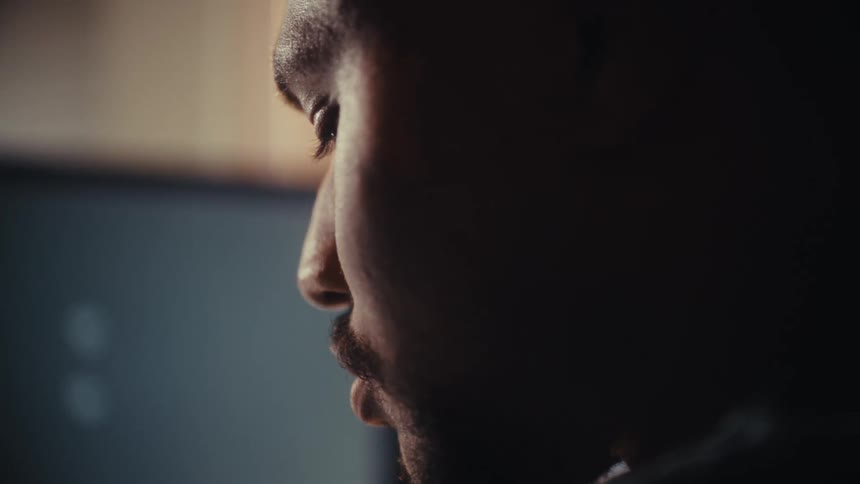Slow-motion close-up shot pans around a focused man looking at a computer screen with tracking markers in a dark, moody room