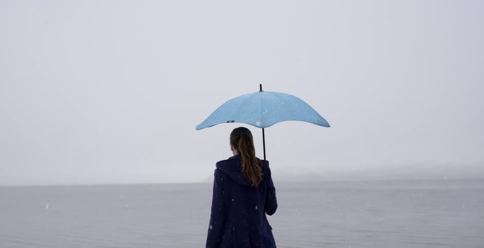 A woman looks out over the water as it snows