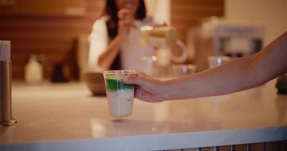Slow motion close-up of a customer's hand picking up a layered iced matcha latte from a modern cafe counter