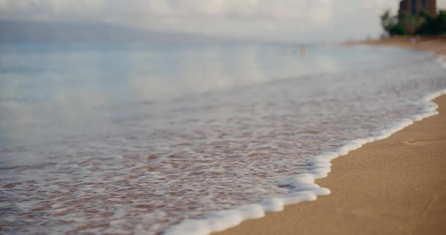 A gentle wave washes ashore in slow motion over the soft sand of a tranquil beach