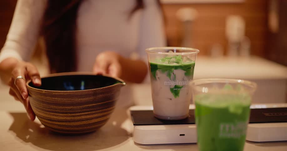 Slow motion close-up of a barista carefully pouring vibrant green matcha tea into a cup of iced milk