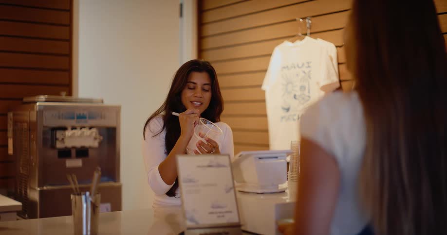 A friendly female employee takes an order from a customer at the counter in a modern frozen yogurt shop