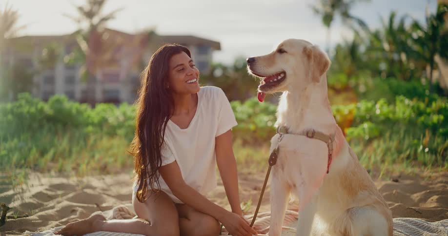 A smiling young woman enjoys a beautiful sunny day on the beach with her adorable golden retriever dog in slow motion