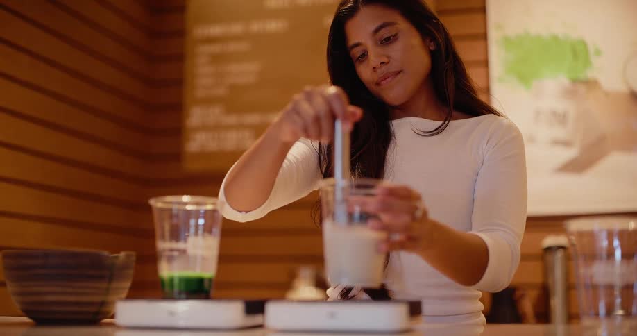 A woman carefully whisks a beverage in a modern cafe in slow motion