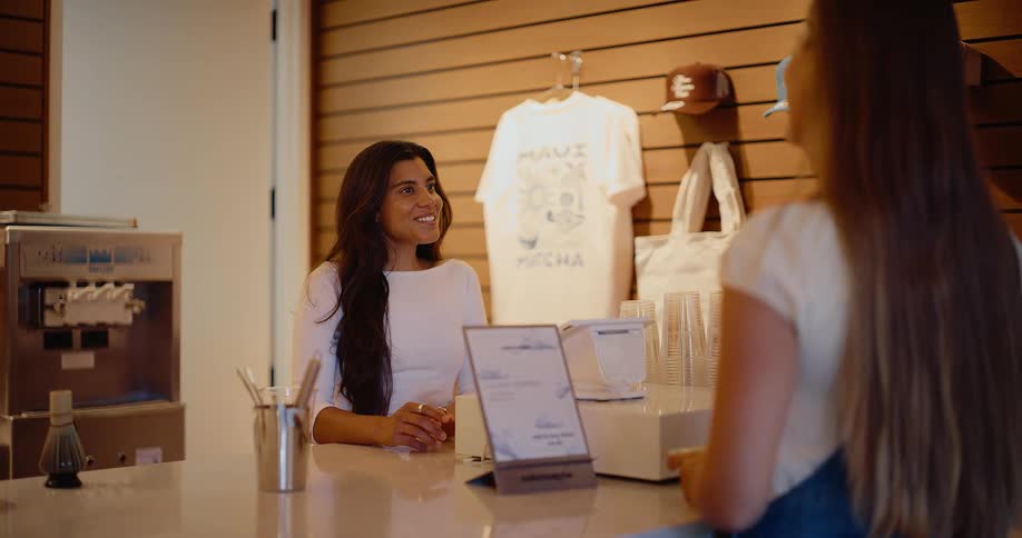 A friendly female barista with a warm smile takes an order from a customer at the counter of a stylish cafe