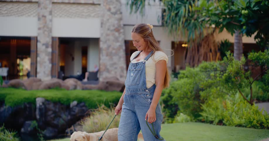 A beautiful woman in overalls happily walks her cute golden lab in slow motion