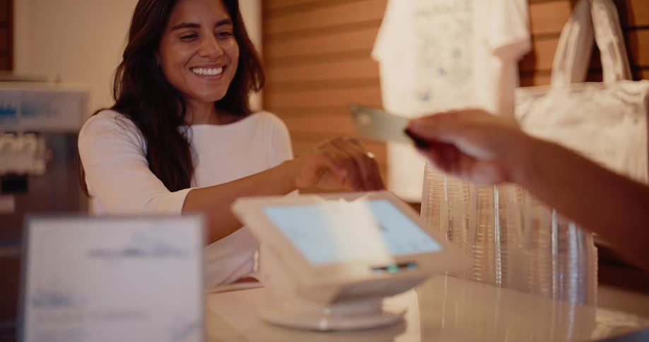 A friendly cashier watches as a customer completes their purchase by making a contactless payment with a credit card on the POS terminal in slow motion