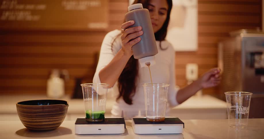 A barista in a modern cafe carefully pours liquid from a squeeze bottle into a cup in slow motion