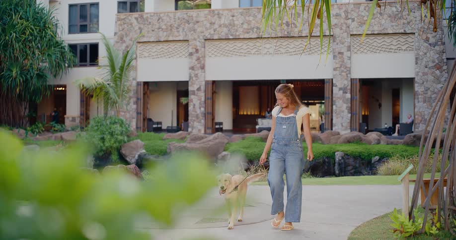 Happy young woman enjoys a leisurely walk with her adorable golden retriever on a beautiful path at a tropical resort