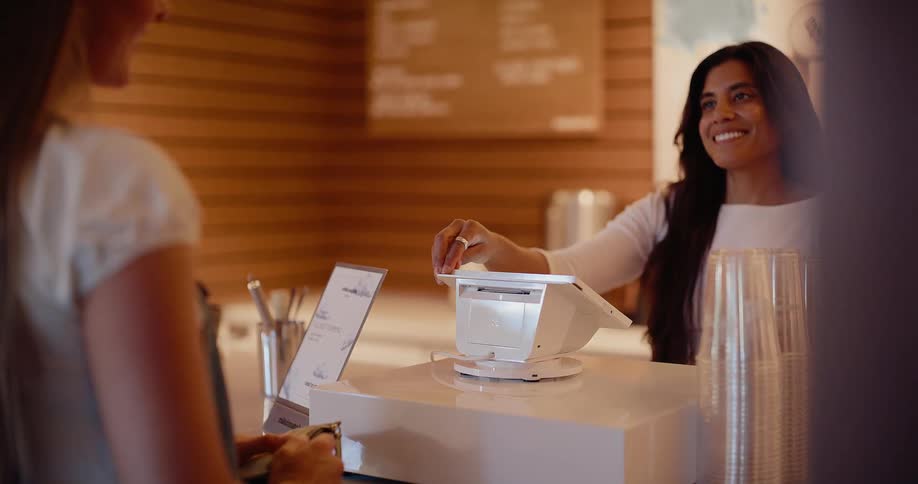 A woman uses a credit card to make a contactless payment on a point-of-sale terminal at a modern cafe counter