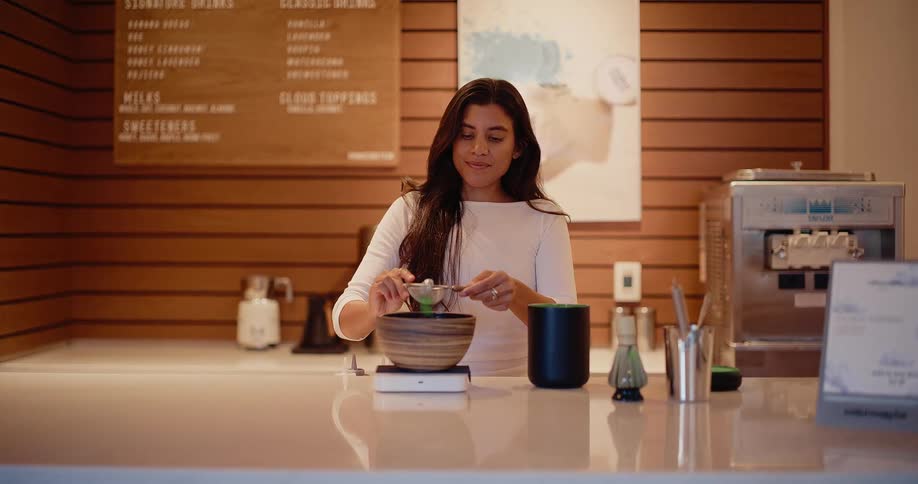 Slow motion dolly-in shot of a barista carefully sifting matcha powder into a bowl in a modern tea shop