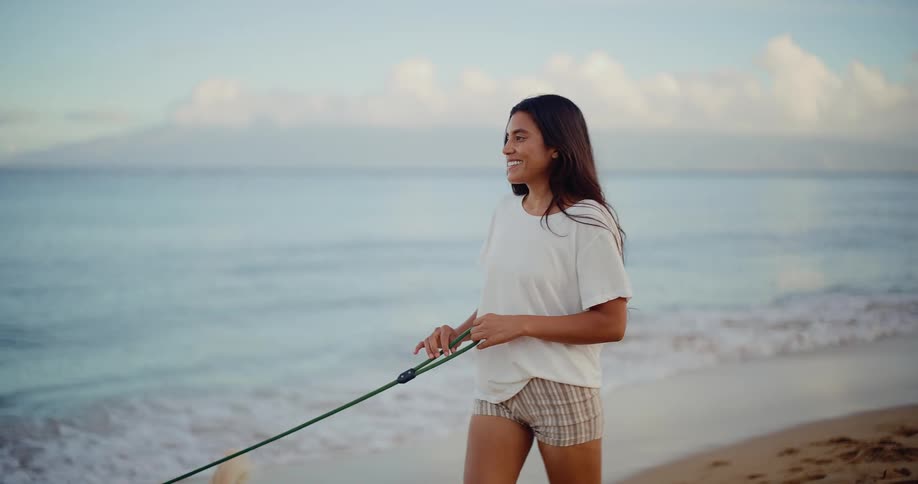A happy young woman walks her dog on the beach at sunrise in slow motion