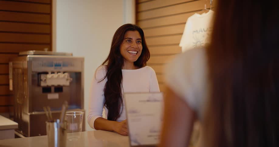 A smiling female employee happily takes a customer's order behind the counter of a modern cafe