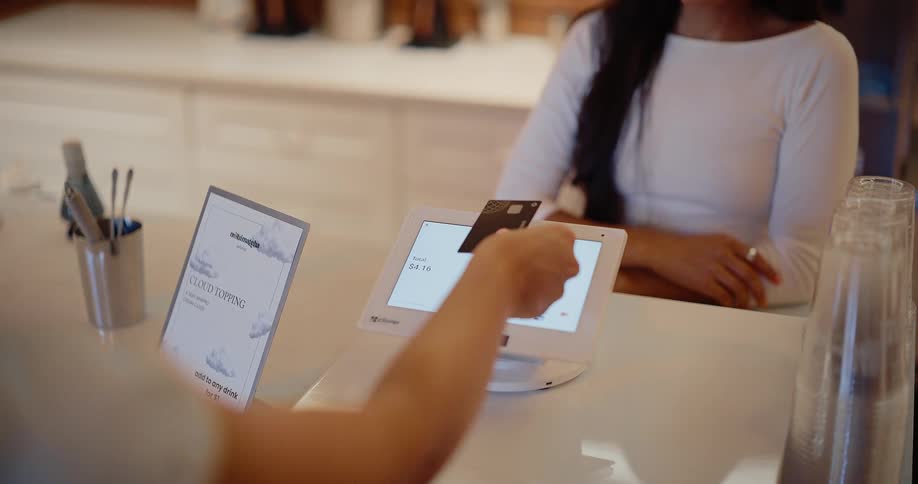 A cashier operates a point-of-sale system as a customer taps their credit card to complete a purchase in a modern cafe