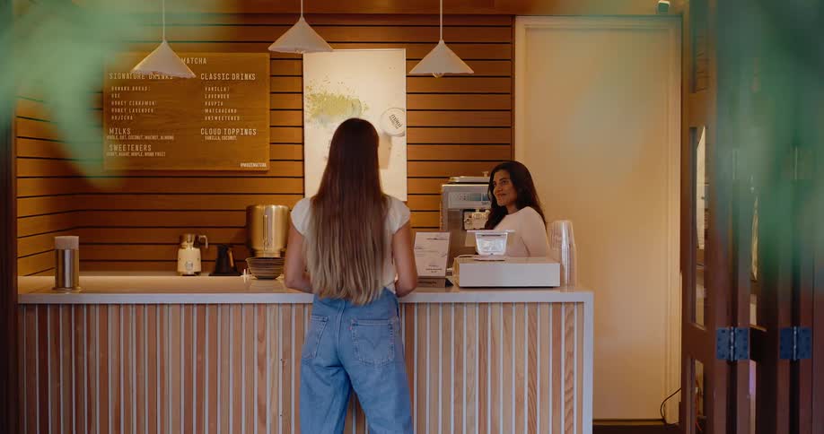 A woman orders a drink from a friendly barista at the counter of a stylish and modern cafe