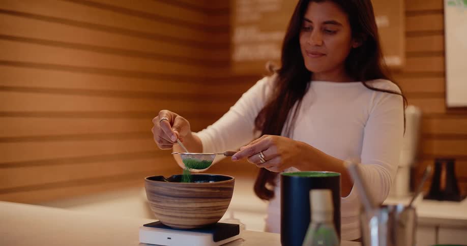 A woman gracefully sifts matcha powder through a sieve into a bowl in super slow motion