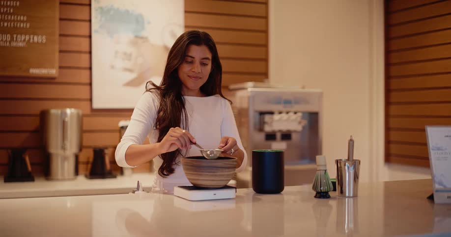 A barista carefully sifts green matcha powder into a traditional bowl in a modern cafe