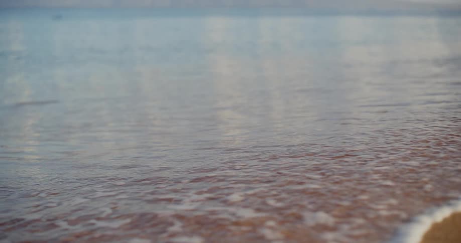 A tranquil ocean wave gently washes over the golden sand in a mesmerizing slow-motion close-up shot