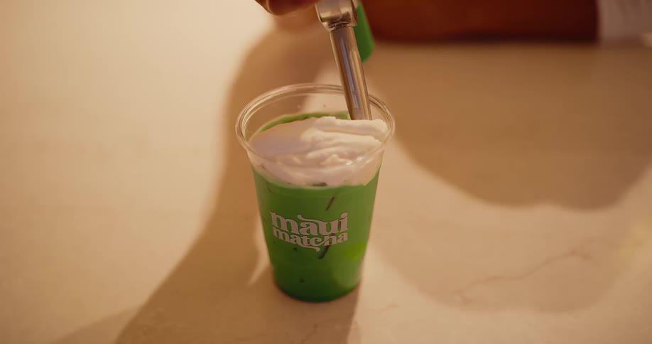Whipped cream is added in slow motion to top a delicious iced Maui Matcha latte